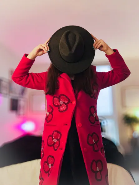 Red coat with flower appliqués and a black wide-brim hat