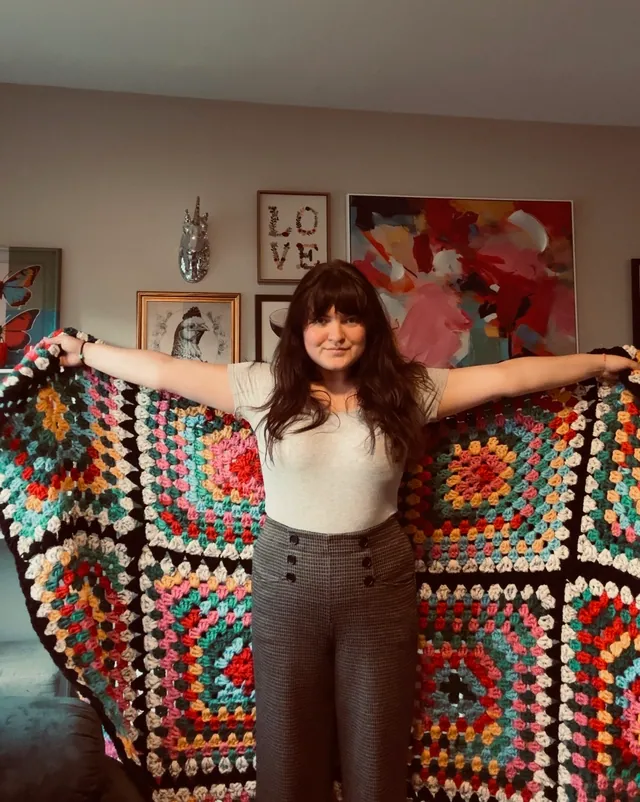 Isabel holding up a large multicolor granny-square blanket
